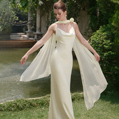 Woman in a flowing white dress standing outdoors near a pond with greenery.