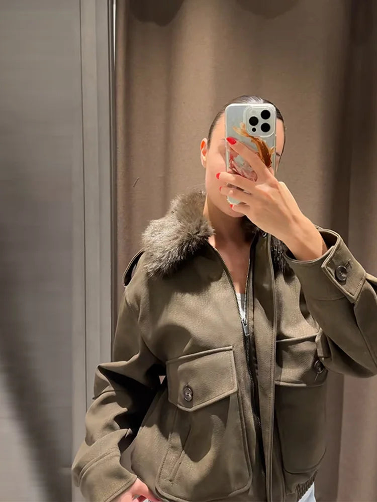 Person wearing a green coat with fur collar taking a mirror selfie.