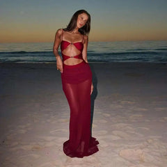 Woman in a red cut-out bikini and sheer maxi skirt on a beach at sunset.