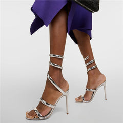 Silver high-heeled sandals worn with a purple skirt on a light gray background