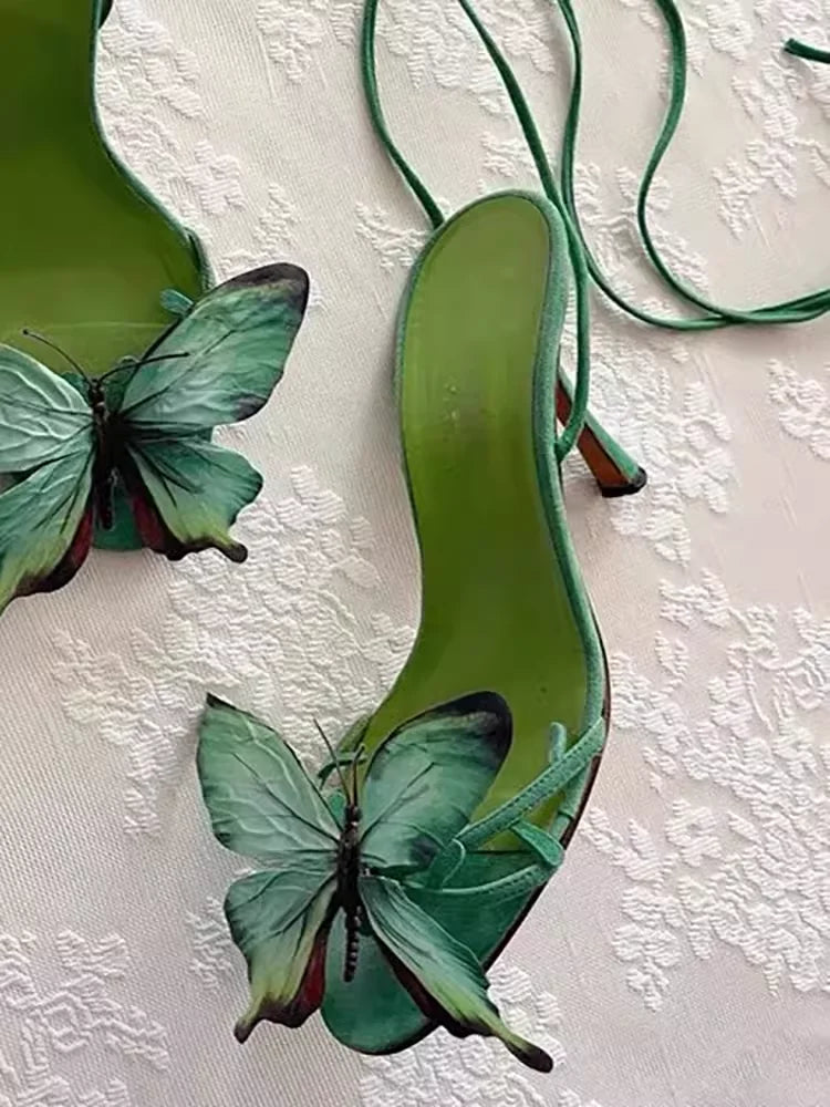 Green high-heeled shoes with butterfly designs on a textured white background