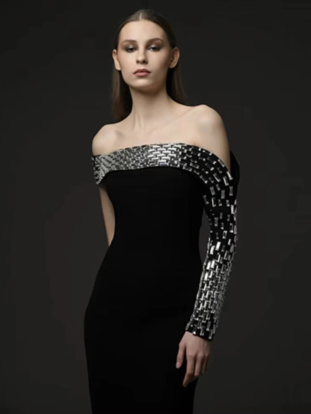 Model wearing a black off-shoulder dress with silver geometric patterns on a dark background