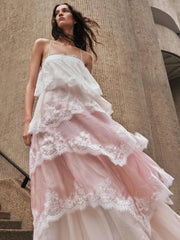 Woman in a white lace dress standing against a beige stone wall.