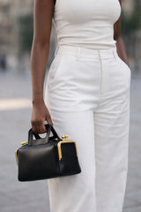 Person wearing a white outfit holding a black handbag with gold accents.