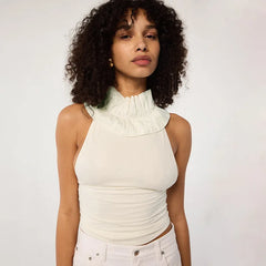 Woman wearing a white sleeveless top with a ruffled neckline against a plain background