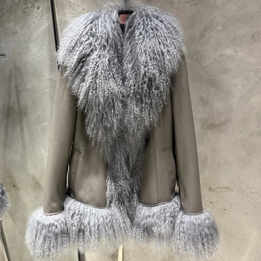 Mannequin wearing a gray leather jacket with a fluffy silver fur trim against a concrete wall.
