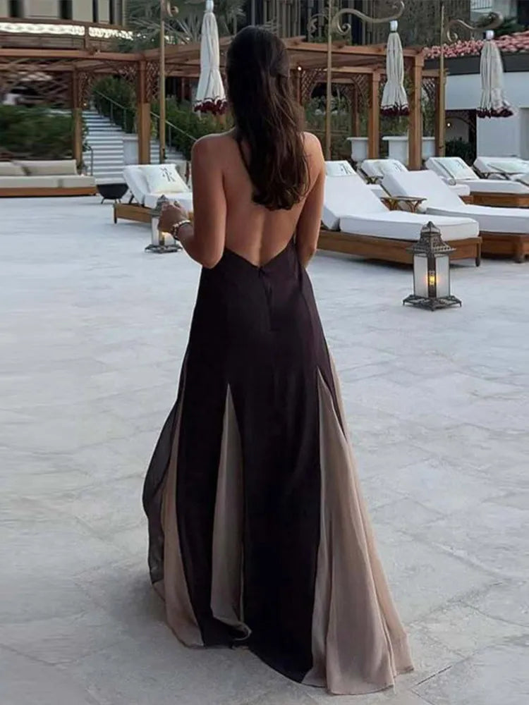 Woman in a long, open-back dress standing on a patio with lounge chairs and umbrellas.