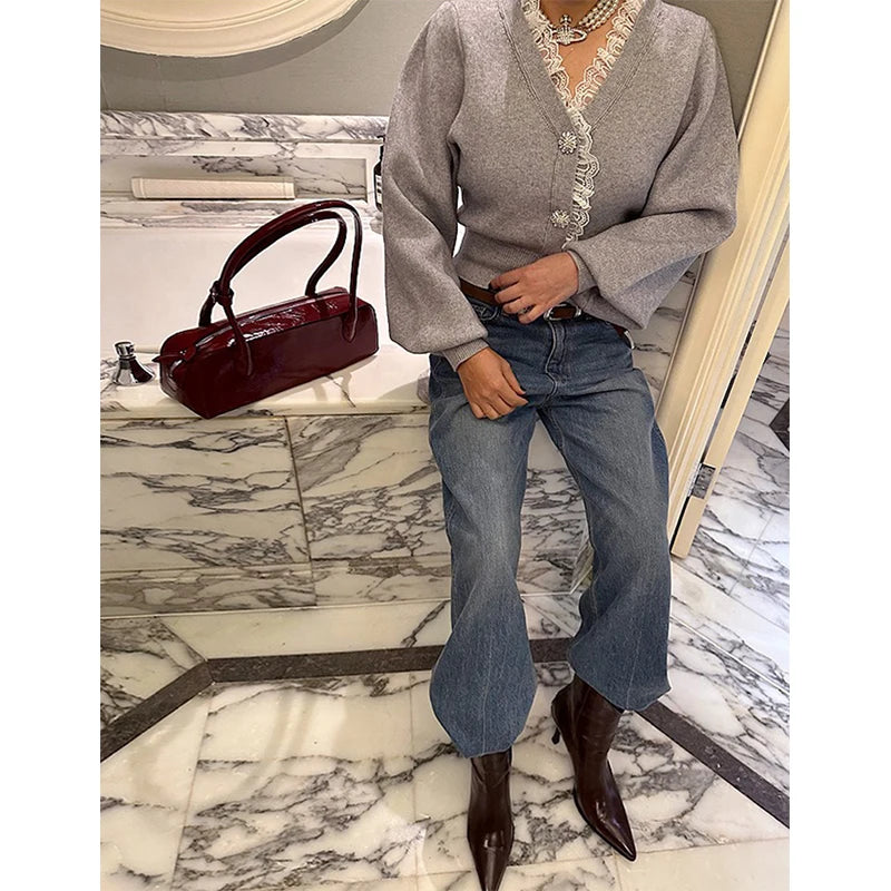 Person wearing a gray sweater and blue jeans, standing on a marble floor with a burgundy handbag.