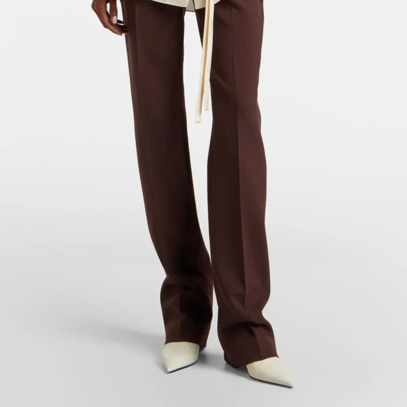 Model wearing white leather pointed toe ankle boots with brown wide-leg trousers.