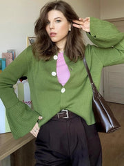 Woman wearing a green cardigan over a pink shirt, holding a brown bag indoors.