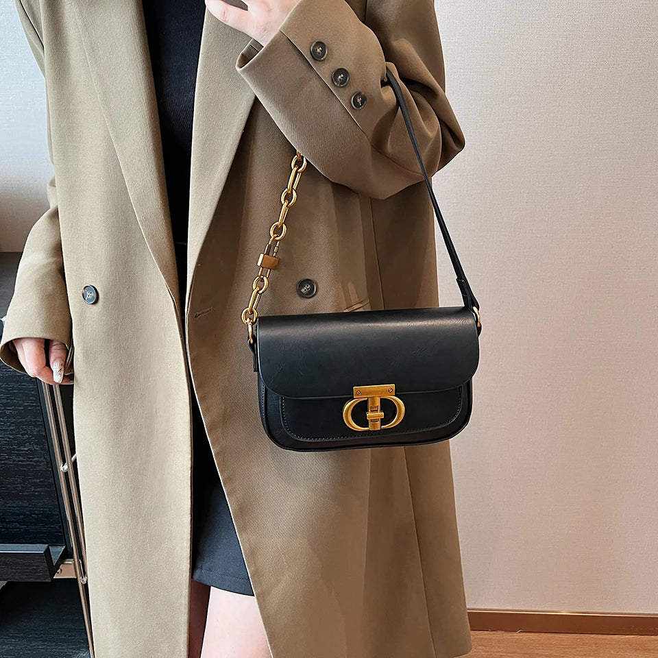 Person wearing a beige coat with a black handbag featuring a gold chain and clasp.