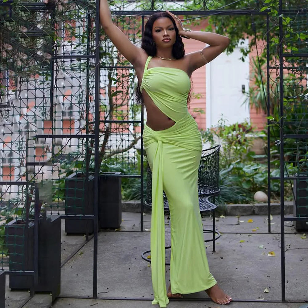 Woman in a bright green dress posing outdoors with plants and a building in the background