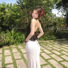 Woman in a black top and white skirt standing in a garden with greenery and flowers.