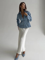 Woman wearing a blue denim jacket and white skirt against a plain background