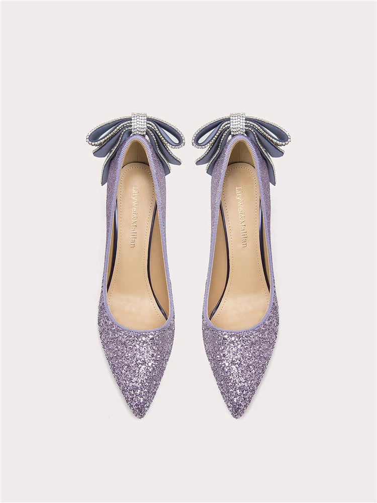 Pair of glittery purple high heels with bow details on a light gray background