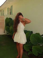 Woman in a white dress standing outdoors with greenery and a house in the background