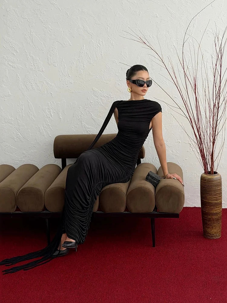 Model sitting in a black pleated sleeveless maxi dress