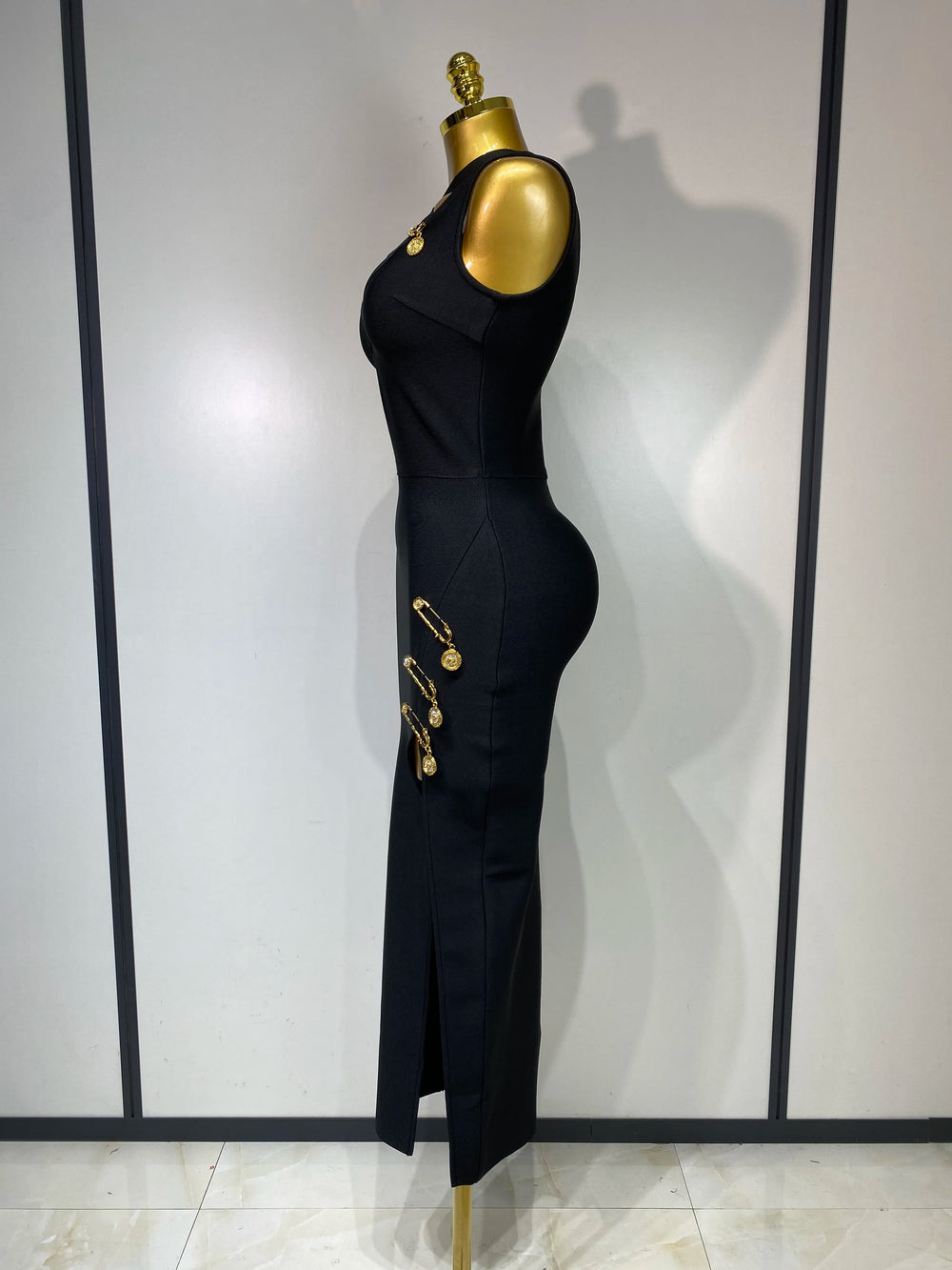 Black dress with gold buttons on a mannequin against a white wall.