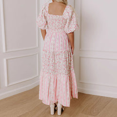 Woman wearing a pink floral dress standing in a room with white paneled walls.
