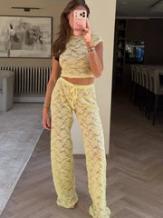 Person wearing a yellow lace cropped t-shirt and wide leg pants in an indoor setting.