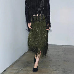 Person wearing a black sequin top and green sequin skirt in an indoor setting.