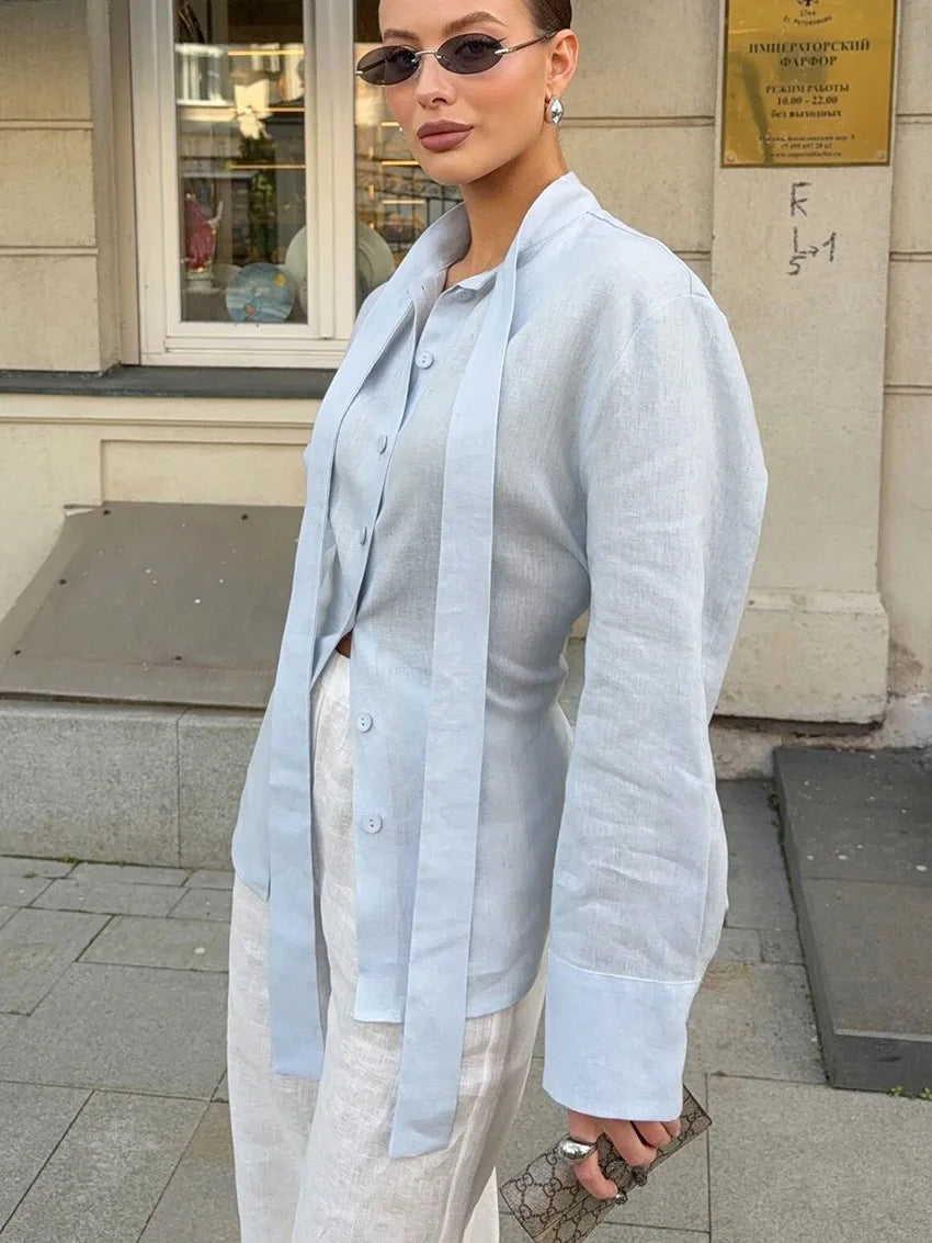 Woman wearing a light blue shirt and white pants standing on a street.