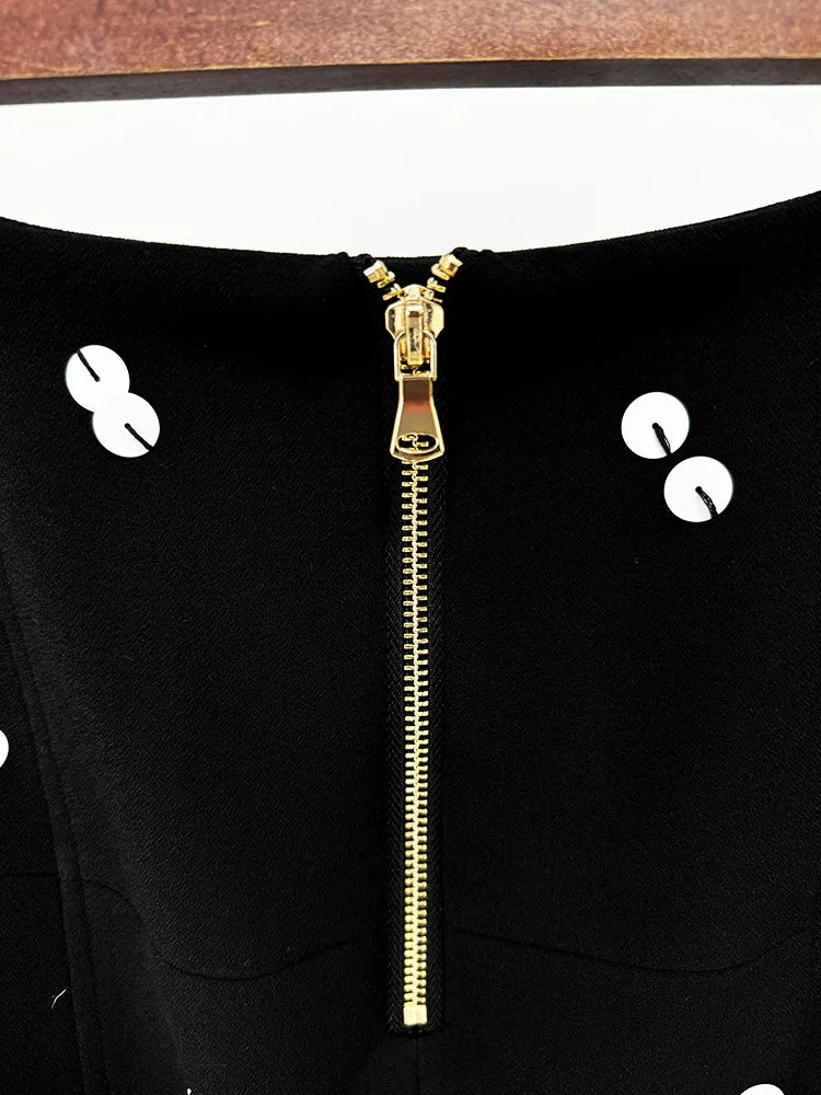 Close-up of a black garment with a gold zipper and white buttons.