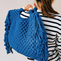 Blue knitted bag with tassels held by a person wearing a striped shirt.