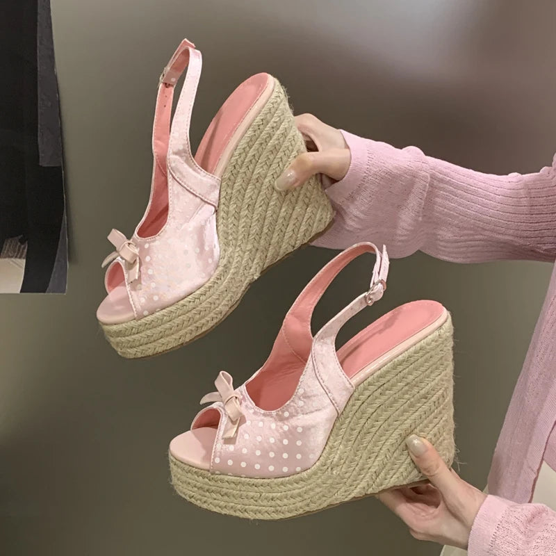 Pink polka dot wedge sandals with jute sole held by a person against a neutral background