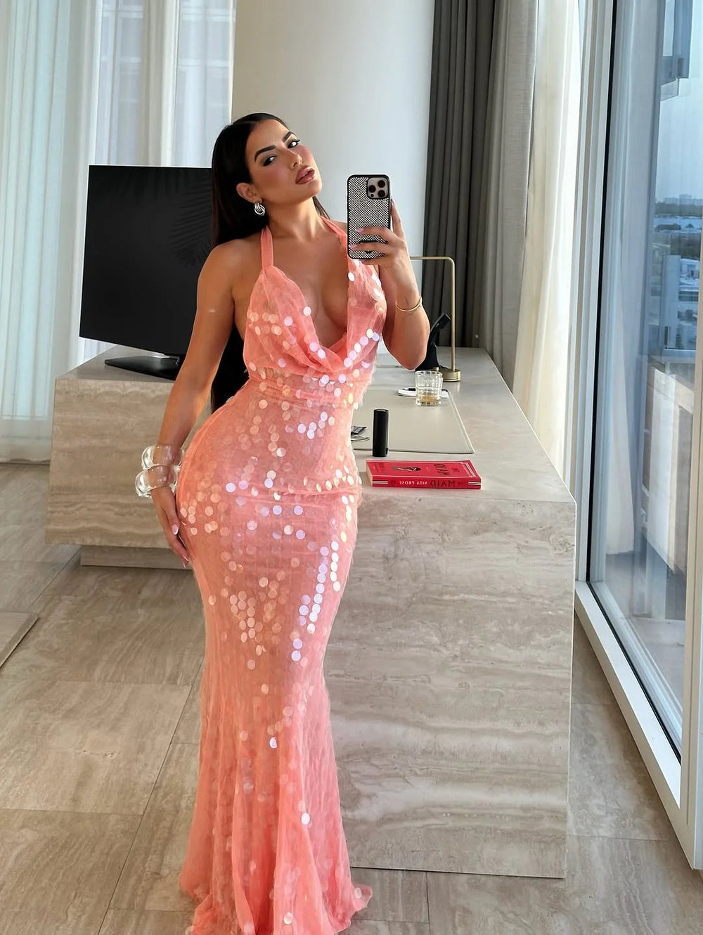 Woman in a pink sequin dress taking a mirror selfie in a modern room.