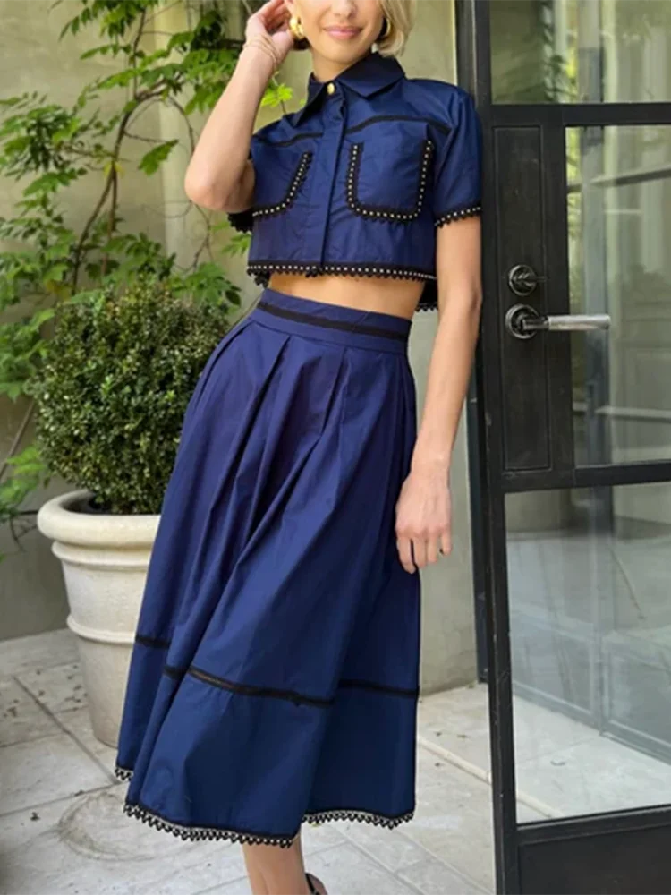 Woman wearing a blue outfit with black trim standing in front of a glass door.