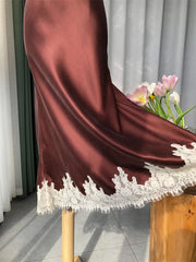Brown satin fabric with white lace trim on a wooden stool, with flowers in the background.