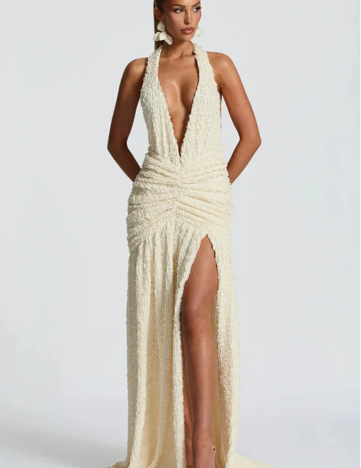 Woman wearing a white evening gown with a deep neckline and high slit on a plain background