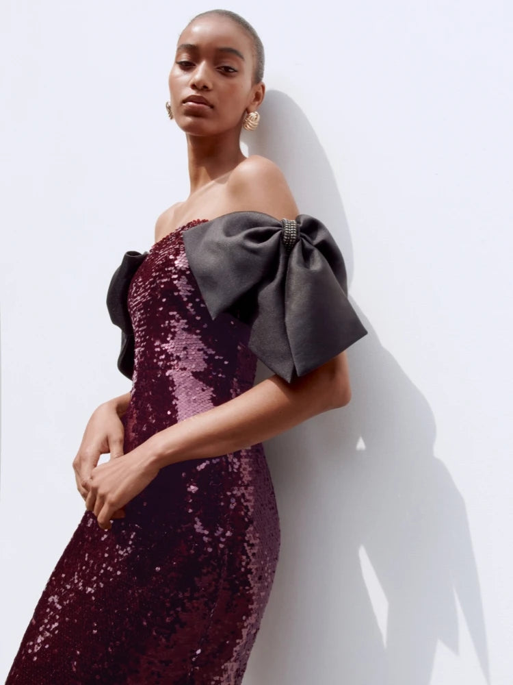 Woman wearing a burgundy sequin dress with a large gray bow on a white background