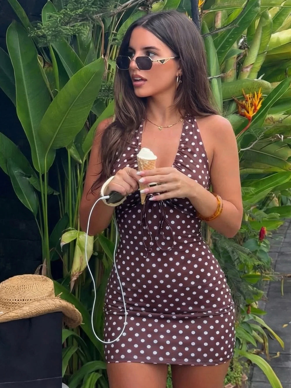 Woman in a polka dot dress holding an ice cream cone amidst green foliage