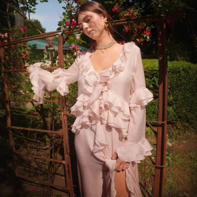 A woman in a pink ruffled dress is standing in a garden with flowers and metal arches.