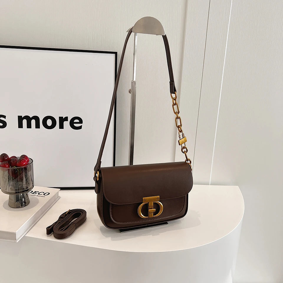 Brown handbag with gold accents on a white surface next to a framed picture and small bowl.