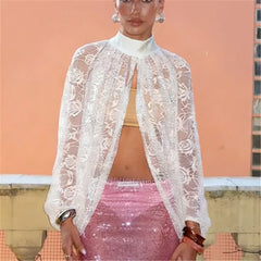 Person wearing a white lace top over a pink skirt with a peach-colored wall background