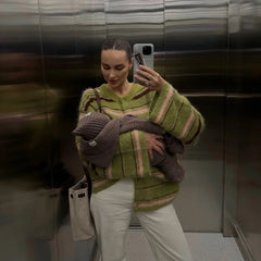 Woman holding a baby while wearing a green striped knit cardigan
