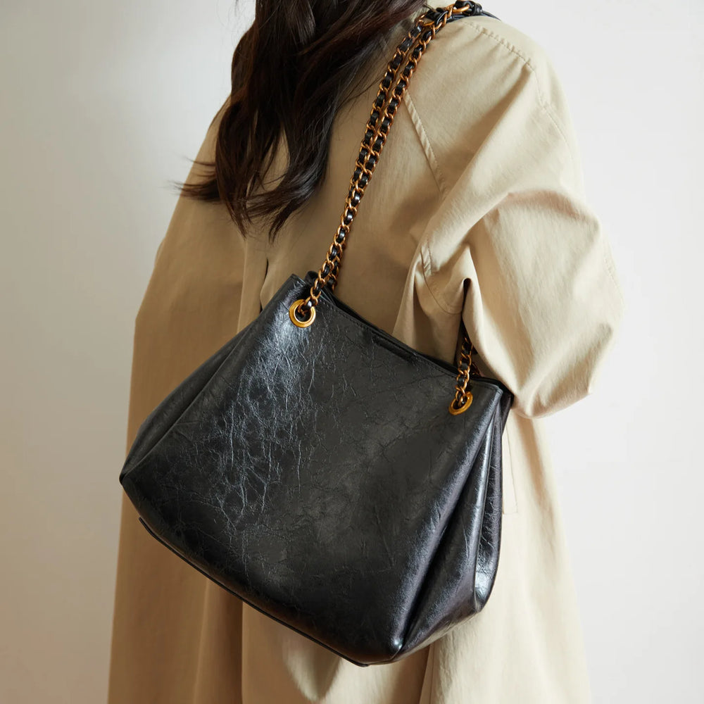 Person wearing a beige outfit with a black handbag featuring a gold chain strap.
