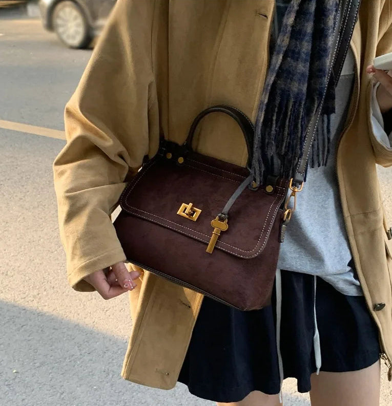 Person wearing a beige coat and holding a brown handbag on a street.