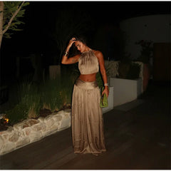 woman posing in a gold halter neck crop top and matching flowing maxi skirt at night