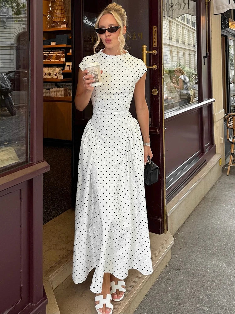 Woman in a white polka dot dress standing outside a store.