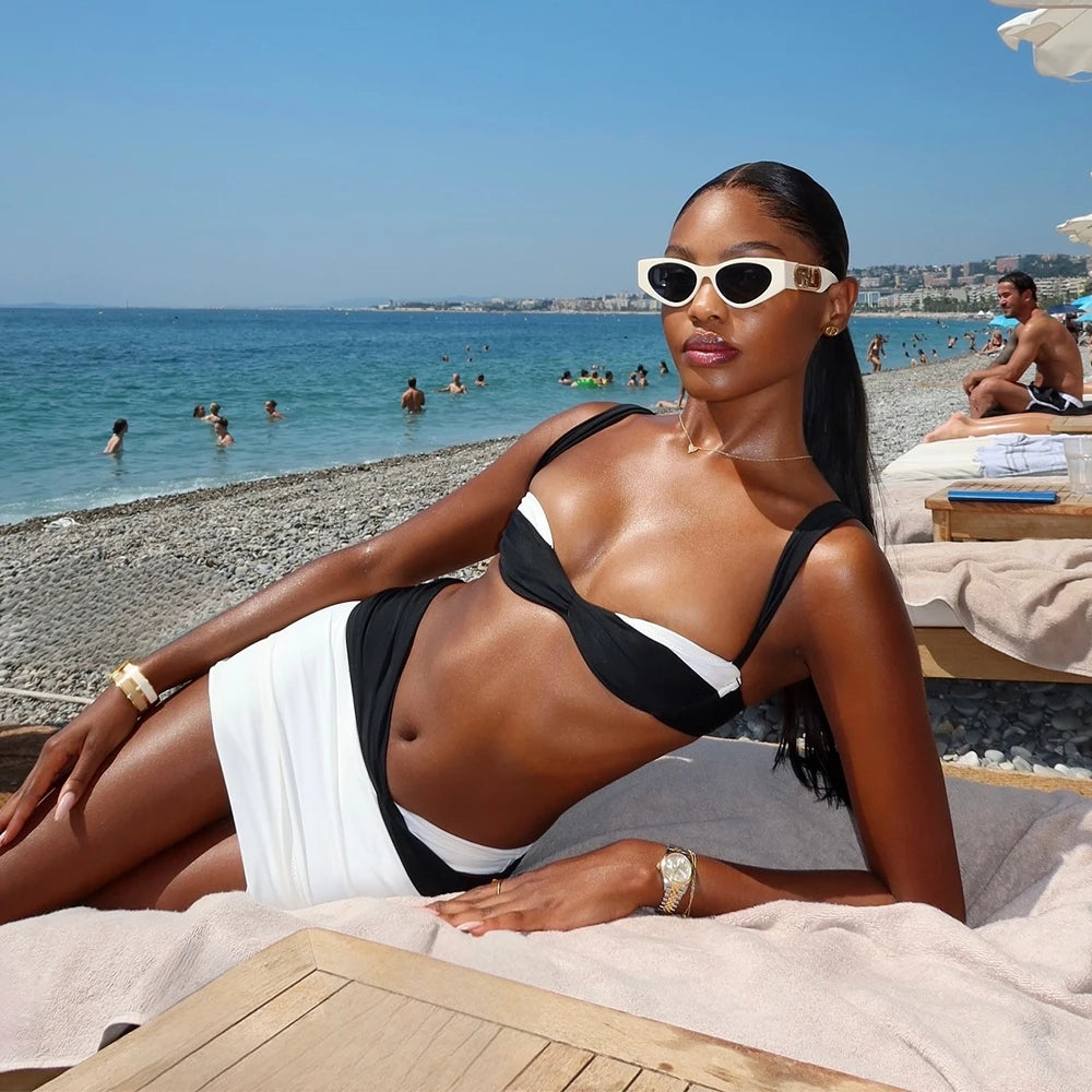 Person wearing a black and white contrast trim bikini top and bottoms with a wrap skirt, leaning against a wooden lifeguard stand.