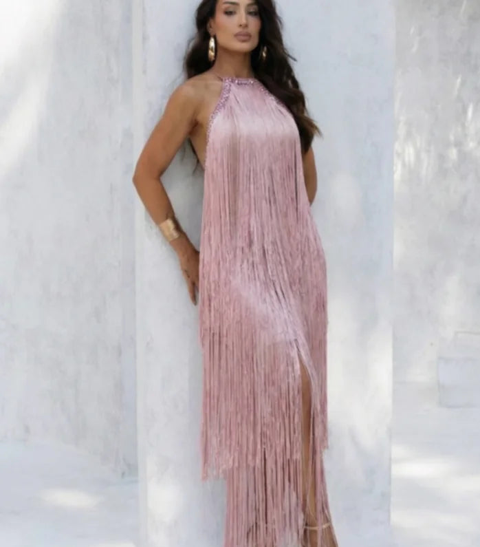 Woman wearing a pink fringe dress against a white wall.
