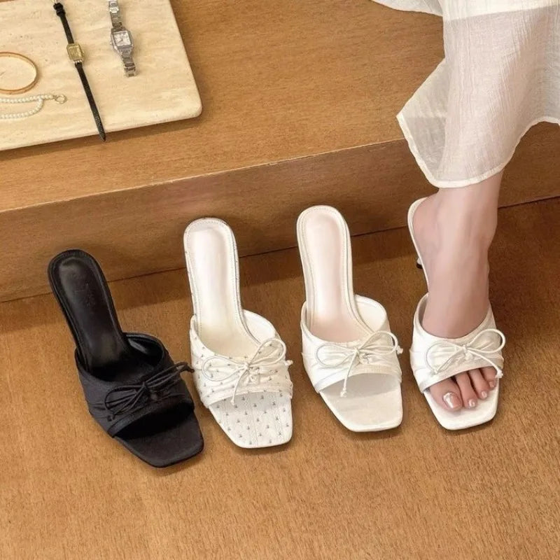 Black and white sandals with bow details on a wooden floor.