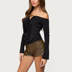 Woman wearing a black off-shoulder top and brown leather shorts on a white background
