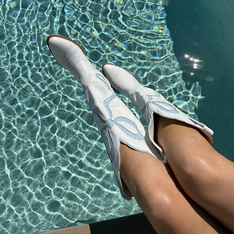 White cowboy boots with blue accents worn by a person by a pool.