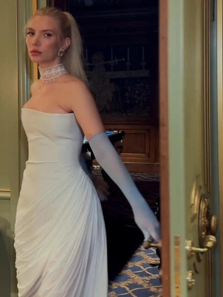 Woman in a strapless white gown with long gloves standing in an elegant room.