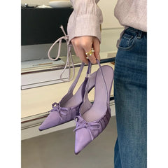 Purple heeled shoes held by a person wearing a beige sweater and blue jeans.